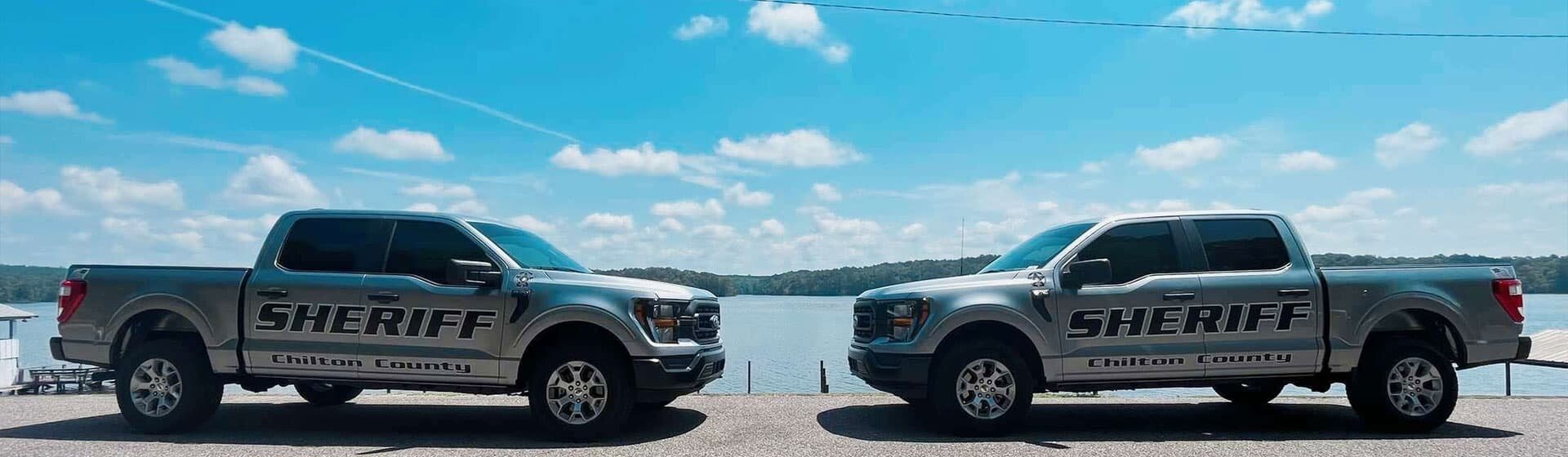 Two Chilton County Sheriff's Office Trucks in front of a lake with a bright clear sky.